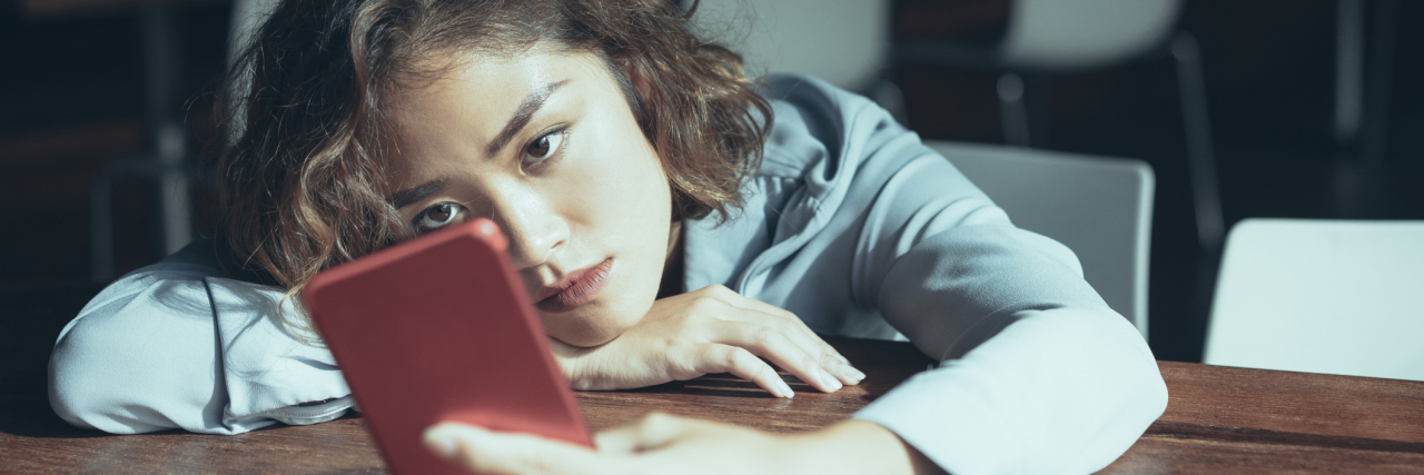 U.K. Wants Rape Survivors to Hand Over Phones or Risk Dropped Charges Closeup of thoughtful young Asian woman leaning on table and surfing Internet on red mobile phone at cafe. Female office worker browsing news feed during break. Mobile communication concept