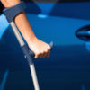 Woman with crutches opening door of car.