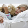a sick girl laying in bed hugging her teddy bear