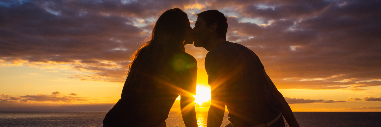 Man and woman sitting by the sea kissing at sunset.