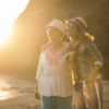 Mother and daughter caucasian people friends at the beach hugging and having fun smiling with golden sun in backlight and ocean in background - family and mixed diversity generations concept