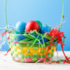 Photo of basket with colorful eggs on blue empty background