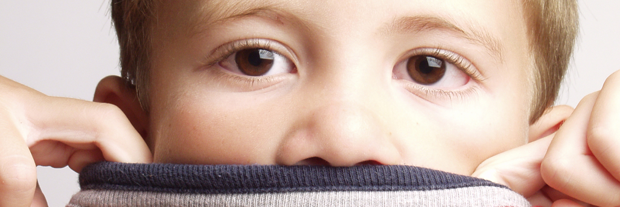 Por Qué los Niños Autistas Verbales a Veces No Pueden Hablar Child covering mouth with red sweater