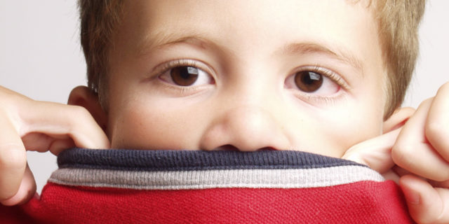 Por Qué los Niños Autistas Verbales a Veces No Pueden Hablar Child covering mouth with red sweater