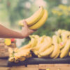 Image of a human hand holding a bunch of ripe bananas on the foreground