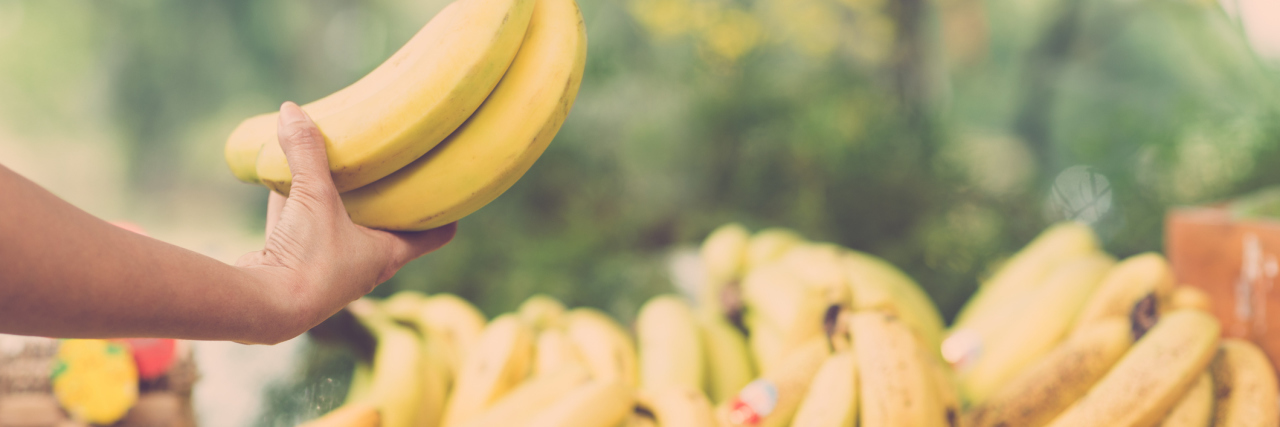 Image of a human hand holding a bunch of ripe bananas on the foreground