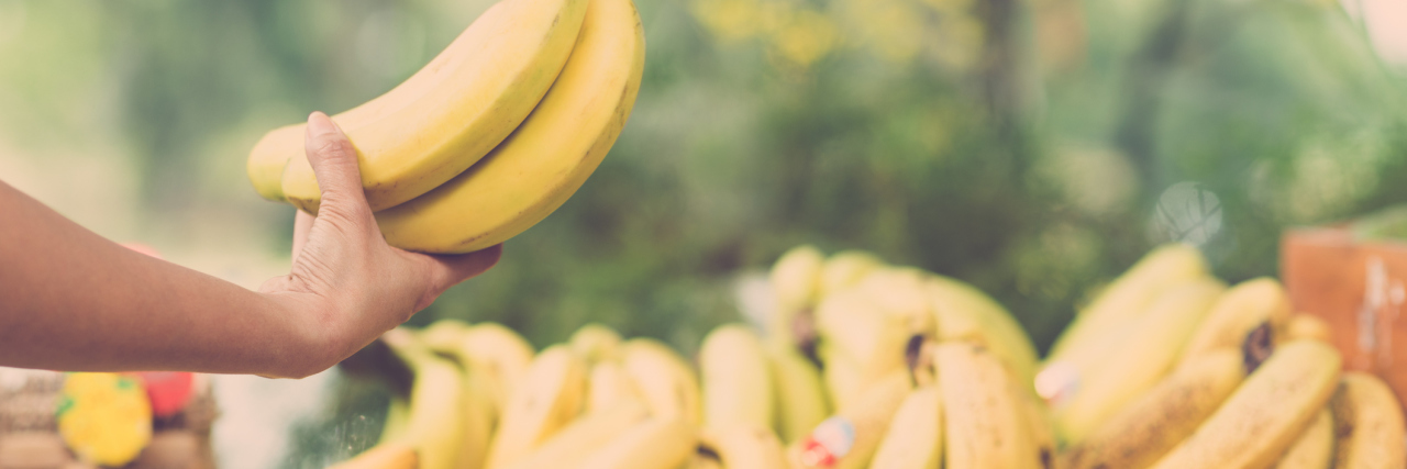 What I Wish I Told the Woman With Cancer at Wegmans Image of a human hand holding a bunch of ripe bananas on the foreground