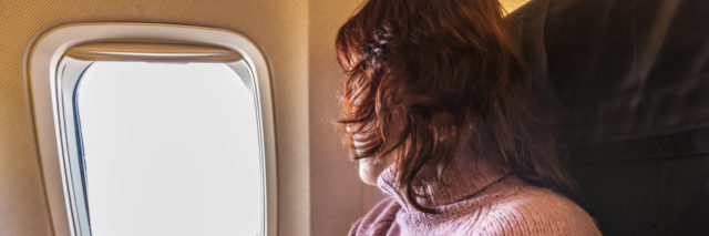 A woman is looking out the window of a plane.