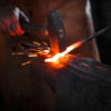 Blacksmith manually forging molten metal.