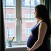 pregnant mother staring out the window, holding her belly