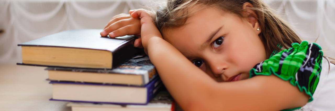 5 Devastating Lies We Learn From 'Narcissistic' Parents A young girl leaning on books, looking sad.