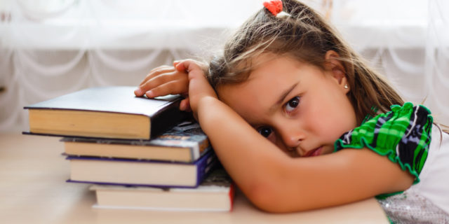 A young girl leaning on books, looking sad.