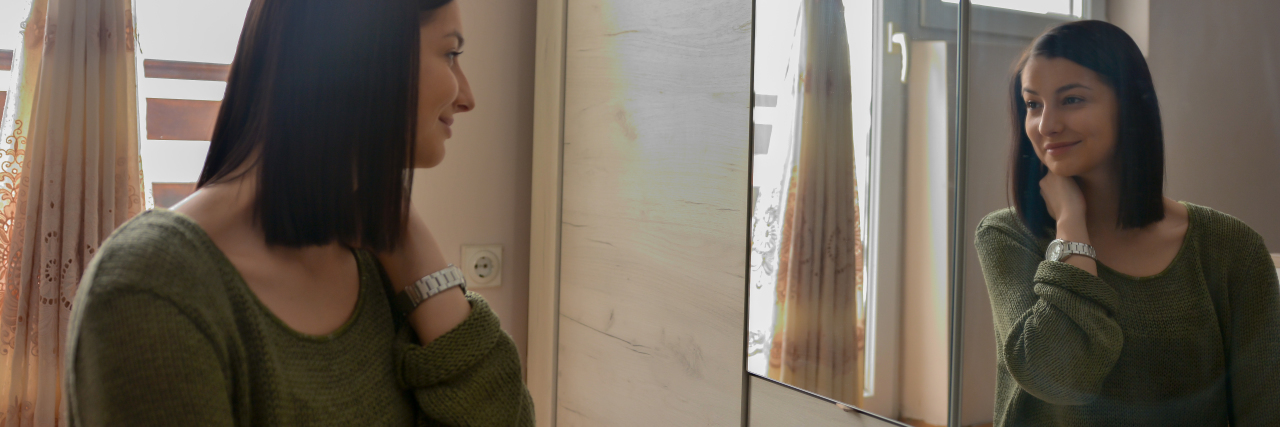 Learning to Love Your Body With Chronic Illness woman looking into mirror and smiling