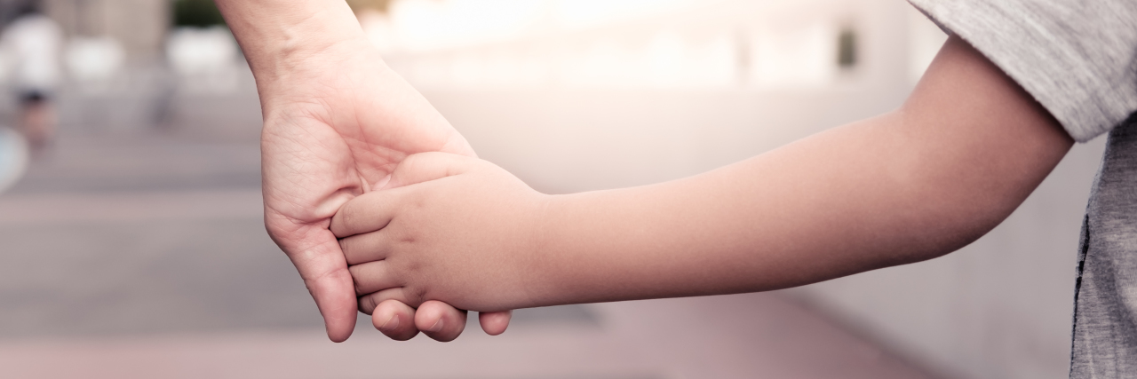 How to Best Support Your Child on the Autism Spectrum Disorder A parent holds the hand of a small boy in the sunset.