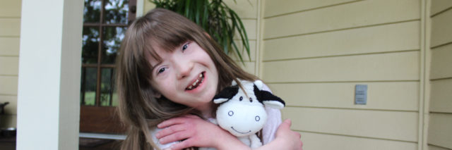 Child with Down syndrome hugging a stuffed cow and smiling at camera