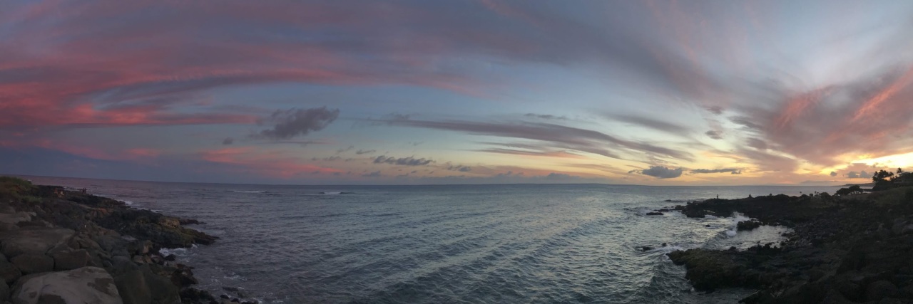 panoramic photo of a sunset over the ocean, taken from the top of a cliff