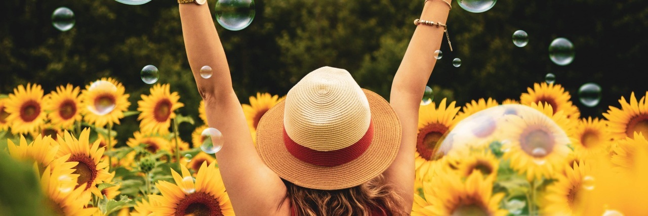 How to Thrive, Not Just Survive, With Chronic Migraine Joyful woman in field of sunflowers.