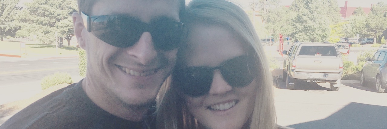 Jess with her husband Jared; they are both wearing sunglasses and smiling.