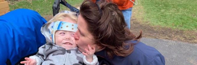 Jennifer Daly kissing her son as he grabs her face and smiles. He is sitting on his wheelchair.