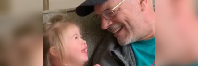 Grandpa playing guitar and looking at his granddaughter who looks up at him with a smile.