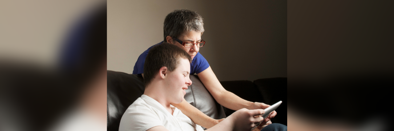 Older mother looking at a tablet with adult son with Down syndrome