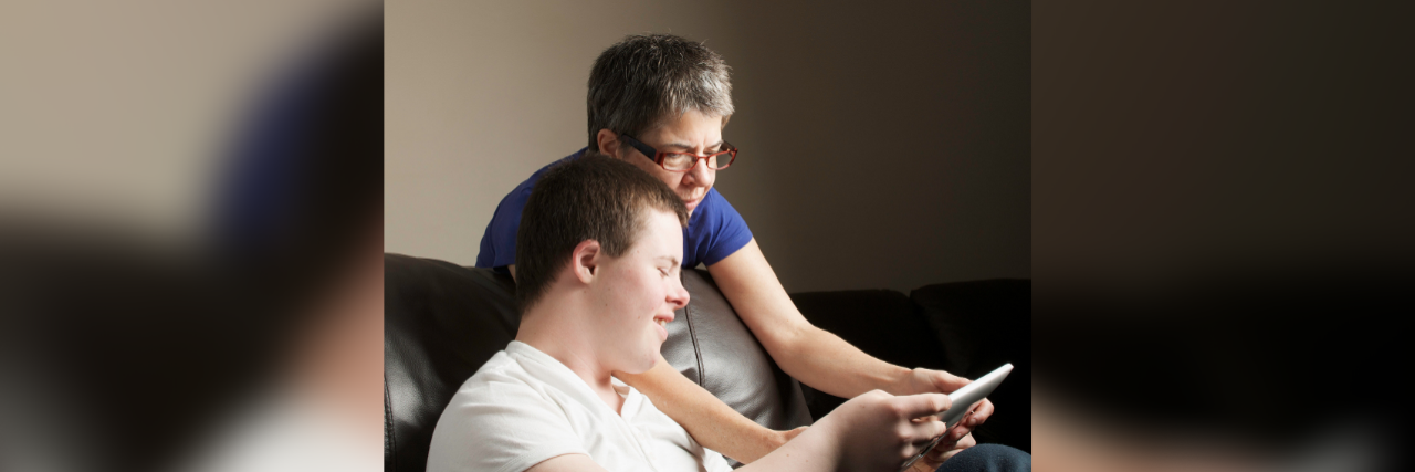 Before Down Syndrome Was Dubbed #TheLuckyFew Older mother looking at a tablet with adult son with Down syndrome