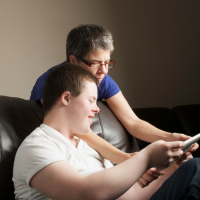 Older mother looking at a tablet with adult son with Down syndrome