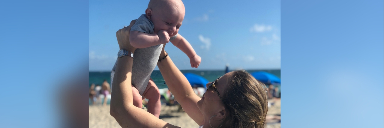 woman holding hp her baby at the beach