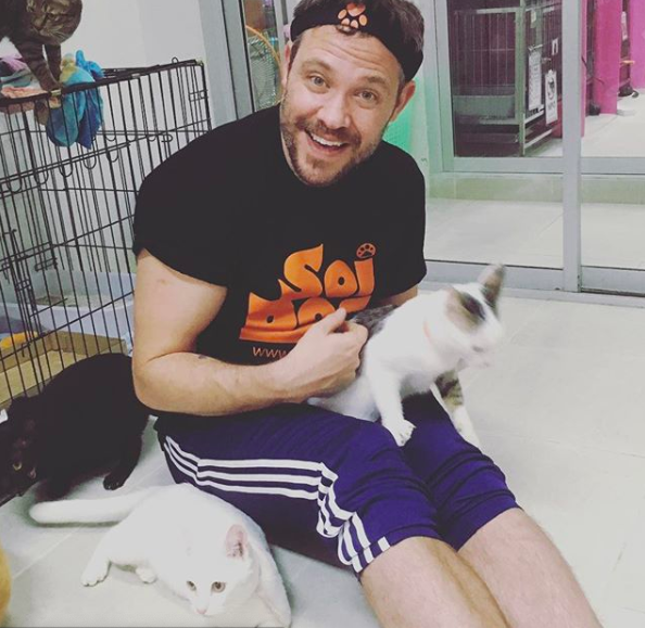 Will Young sitting on the floor holding and surrounding by cats.