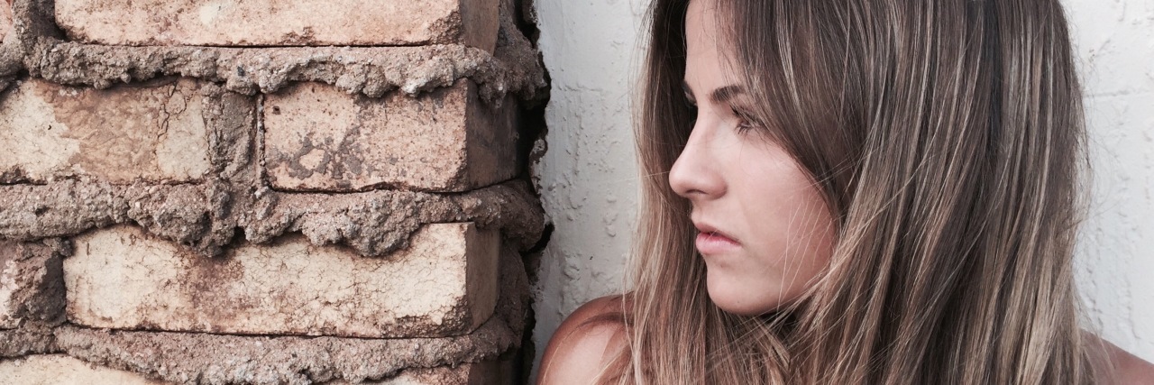 How My Eating Disorder Promised to Protect Me From Abuse photo of woman with long hair standing beside brick wall looking off to side as if in fear