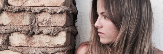 photo of woman with long hair standing beside brick wall looking off to side as if in fear
