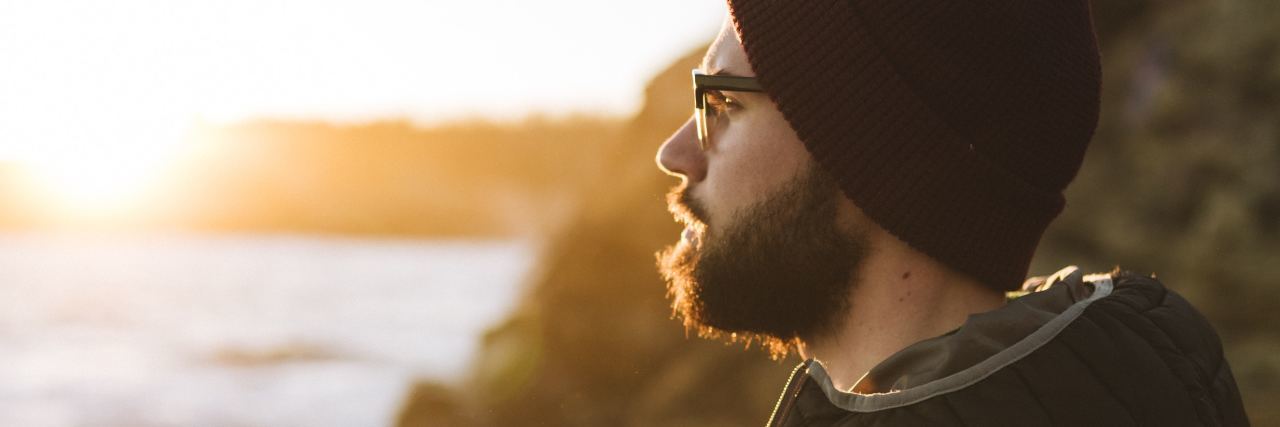 Having Obsessive-Compulsive Disorder Thoughts on Vacation photo of man with beard wearing coat and hat and looking out over sea at sunset or sunrise
