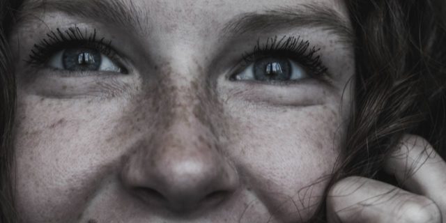 close up photo of young woman with genuine smile and hand raised to cheek