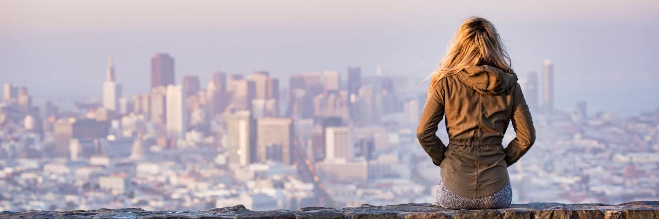 Why I Went From Melanoma Survivor to Feeling Like a Cancer Patient woman sitting on ledge looking at city skyline