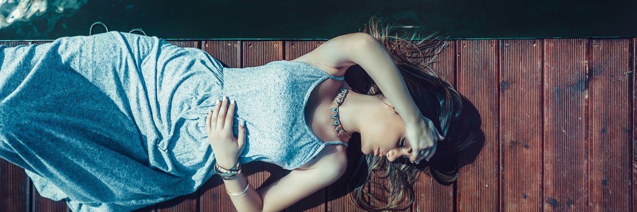 My Answer to the Question 'What Is Your Migraine Story?' photo of woman lying on wooden dock covering eyes with arm