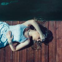 photo of woman lying on wooden dock covering eyes with arm