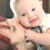 Mom kissing adorable baby boy with Down syndrome who is smiling at the camera