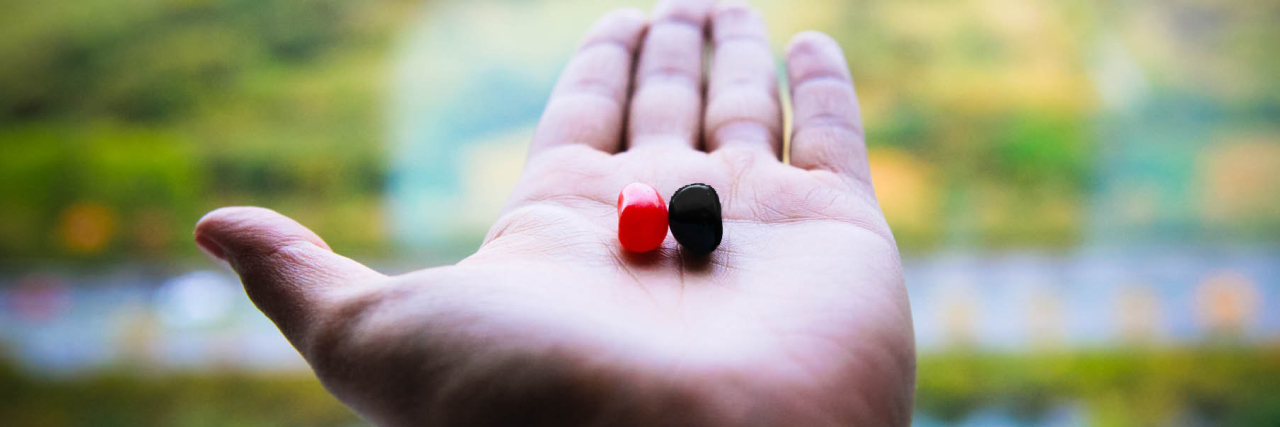 close up photo of man's hand holding one red and one black jelly bean candy