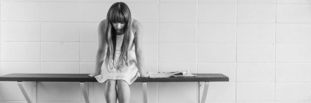 black and white photo of lonely girl sitting on bench against wall looking depressed