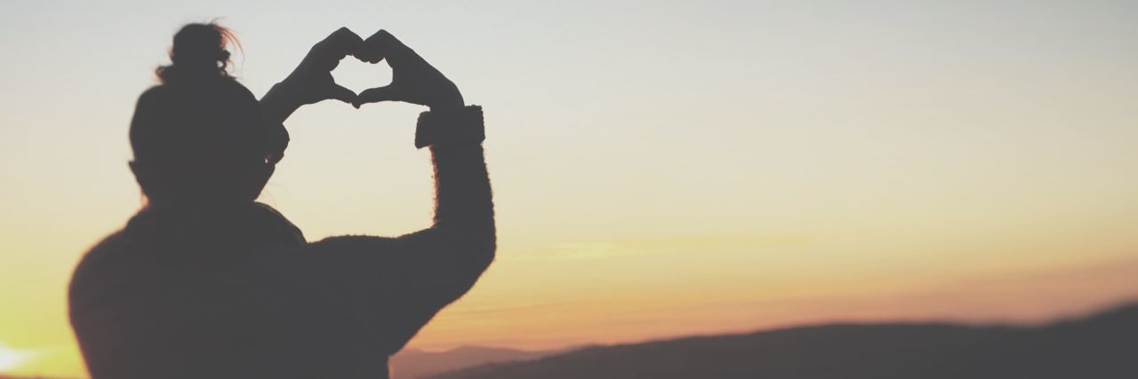 The Positive Life Changes That Came With My Chronic Illness photo of woman making heart shape with hands silhouetted against sunset