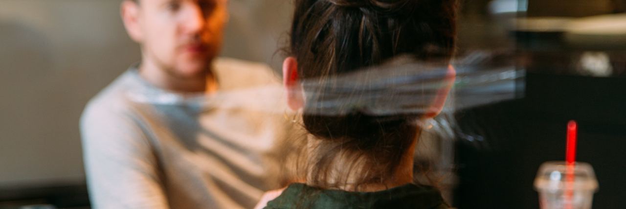 Should I Tell People About My Trauma? photo taken from behind woman sitting in front of slightly blurred man in conversation behind glass at office table