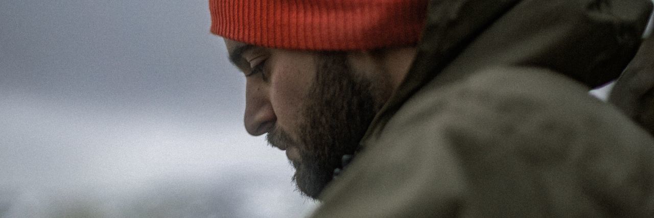 What to Know About People Who Died by Suicide photo of man wearing red hat with his eyes lowered in sadness or mourning