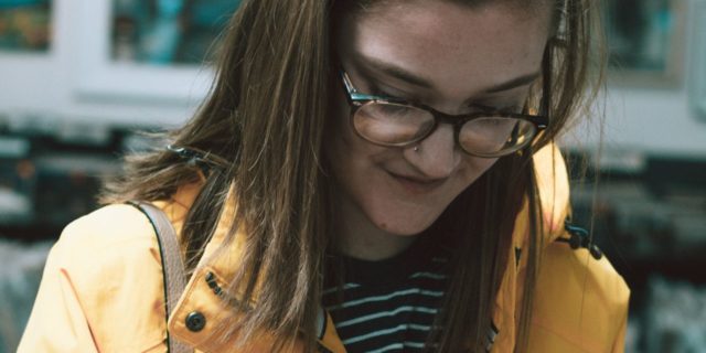 photo of geek girl wearing glasses and yellow coat looking down at LP vinyl