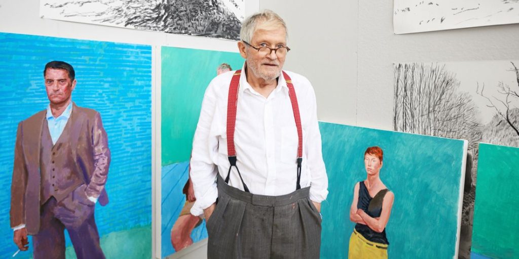 David Hockney standing in front of his paintings