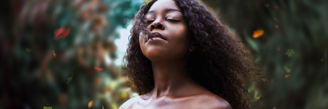 photo of black woman standing among falling leaves with eyes closed and head raised to the sky