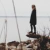 Phoyo of woman standing on rock or log beside lake on cloudy day looking out over water