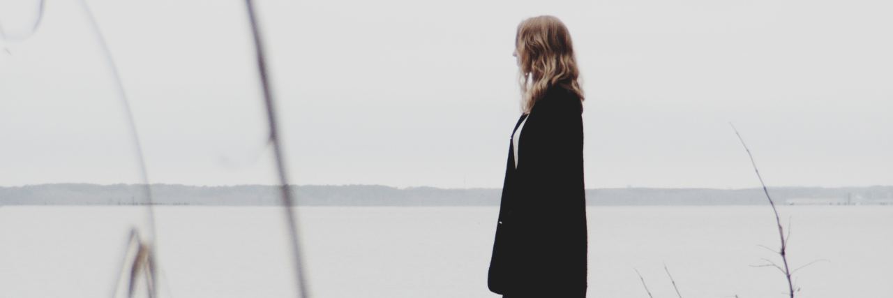 Things I've Learned About Living With Fibromyalgia Phoyo of woman standing on rock or log beside lake on cloudy day looking out over water