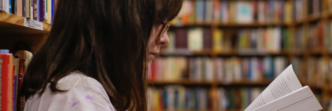 Read This If Nobody Knows You’re Struggling in High School Like I Am photo of young high school student with dark hair and glasses reading book alone in library