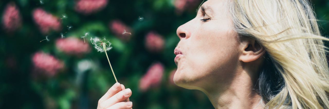 photo of blonde woman blowing dandelion seeds making a wish