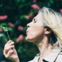 photo of blonde woman blowing dandelion seeds making a wish